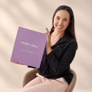 A smiling woman in a black blouse and pale pink pants sits in a chair holding a large lavender-purple square box printed with the brand name 'MODE & OPAL' and the signature 'Kim Christensen'. The background is a soft beige studio backdrop with subtle shadowing.