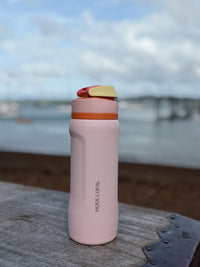Petal Pink Mode & Opal drink bottle resting on a rock by the sea.