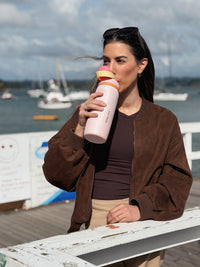 Woman drinking from a Petal Pink Mode & Opal drink bottle at a marina.