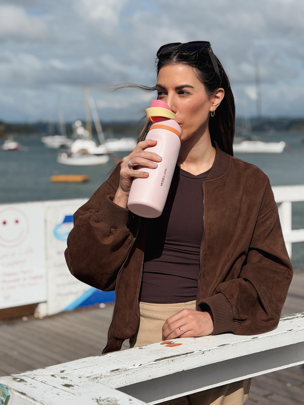 Woman drinking from a Petal Pink Mode & Opal drink bottle at a marina.