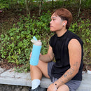 A person sitting outdoors on a stone ledge in a wooded area, holding a light blue water bottle. The image includes overlaid fitness text showing distance, pace, time, and a route labeled STRAVA.